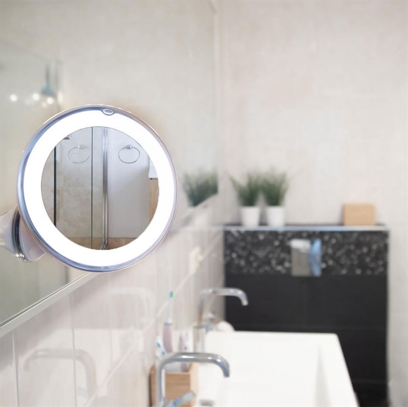 A close-up of the UNIQ PRO BEAUTY Bathroom Mirror with LED Light and Suction Cup x10 Magnifying Mirror in white, wall-mounted in a modern bathroom with double sinks, potted plants, and a black countertop.