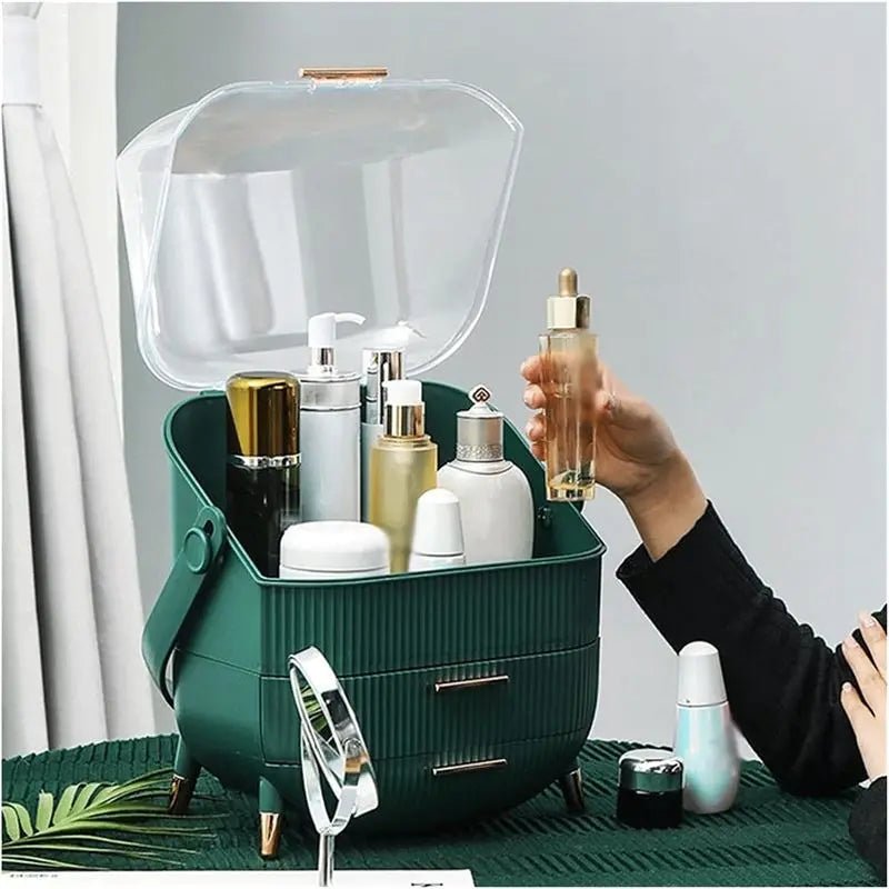 A person holds a dropper bottle above an open UNIQ Retro Makeup Box Organiser (Dark Mint / Dark Green) by UNIQ, filled with skincare and beauty products on a green table, alongside other visible bottles and containers.