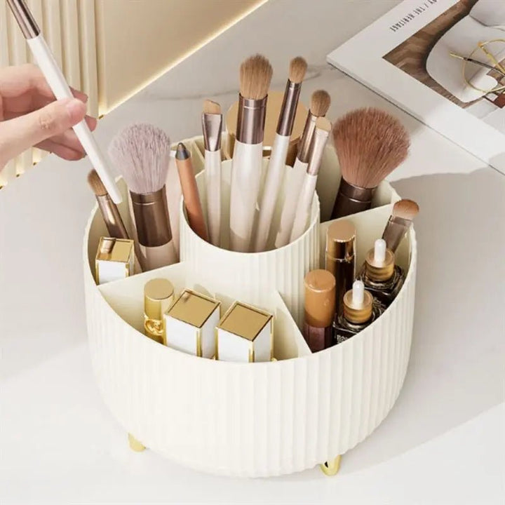 The UNIQ Rotating Makeup Organiser in Cream White by UNIQ holds makeup brushes, lipsticks, and cosmetics. A hand selects a brush as the organiser sits on a light surface near an open magazine, providing stylish storage.