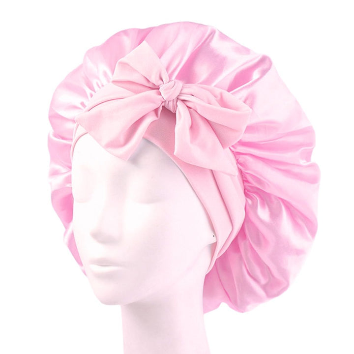 The SOHO Makena Satin Bonnet - Pink by Fashiongirl, shown on a mannequin head, features a shiny pink satin finish and large front bow—ideal for hair protection and frizz prevention.